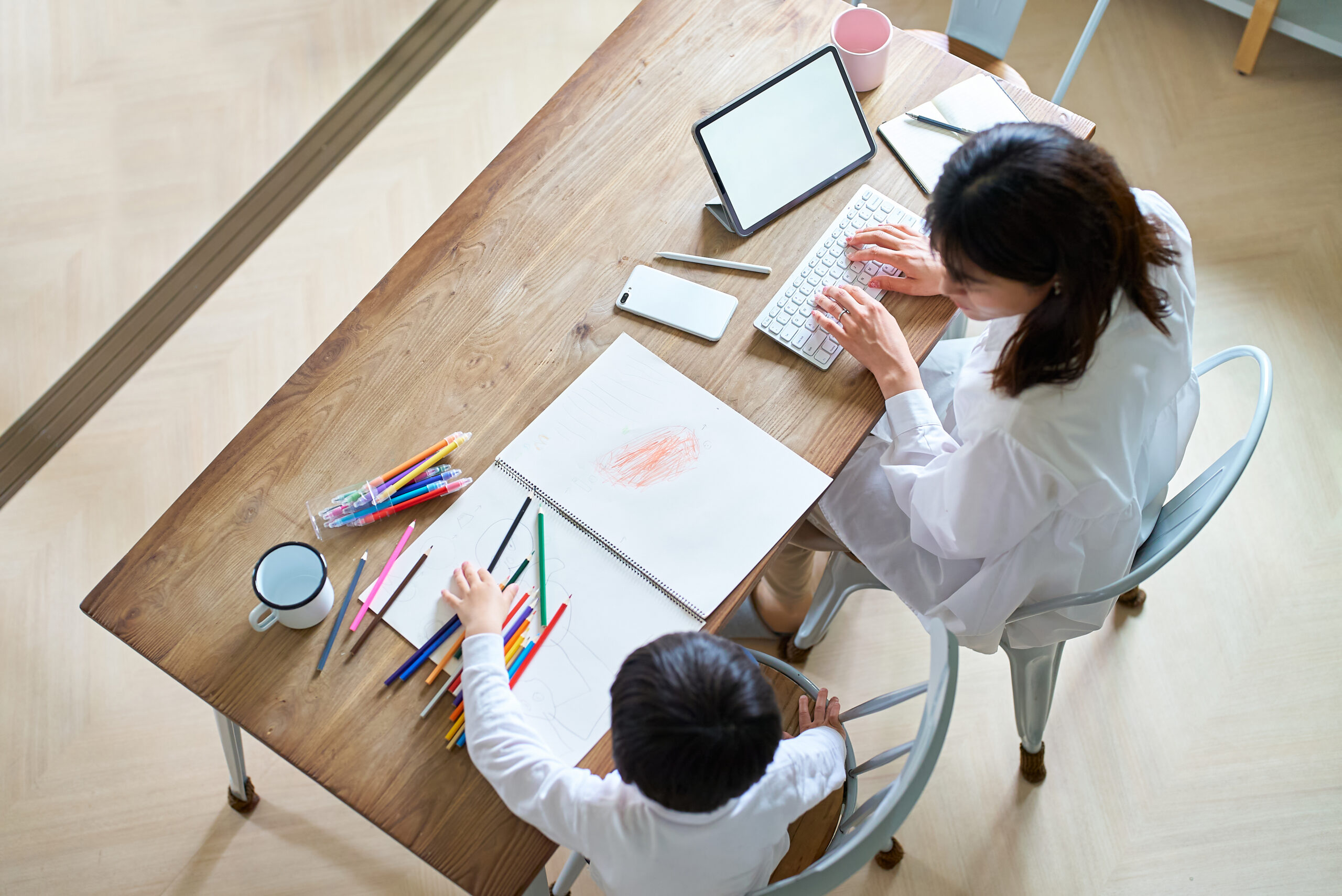 部屋で仕事をする母親と、お絵描きをする子供